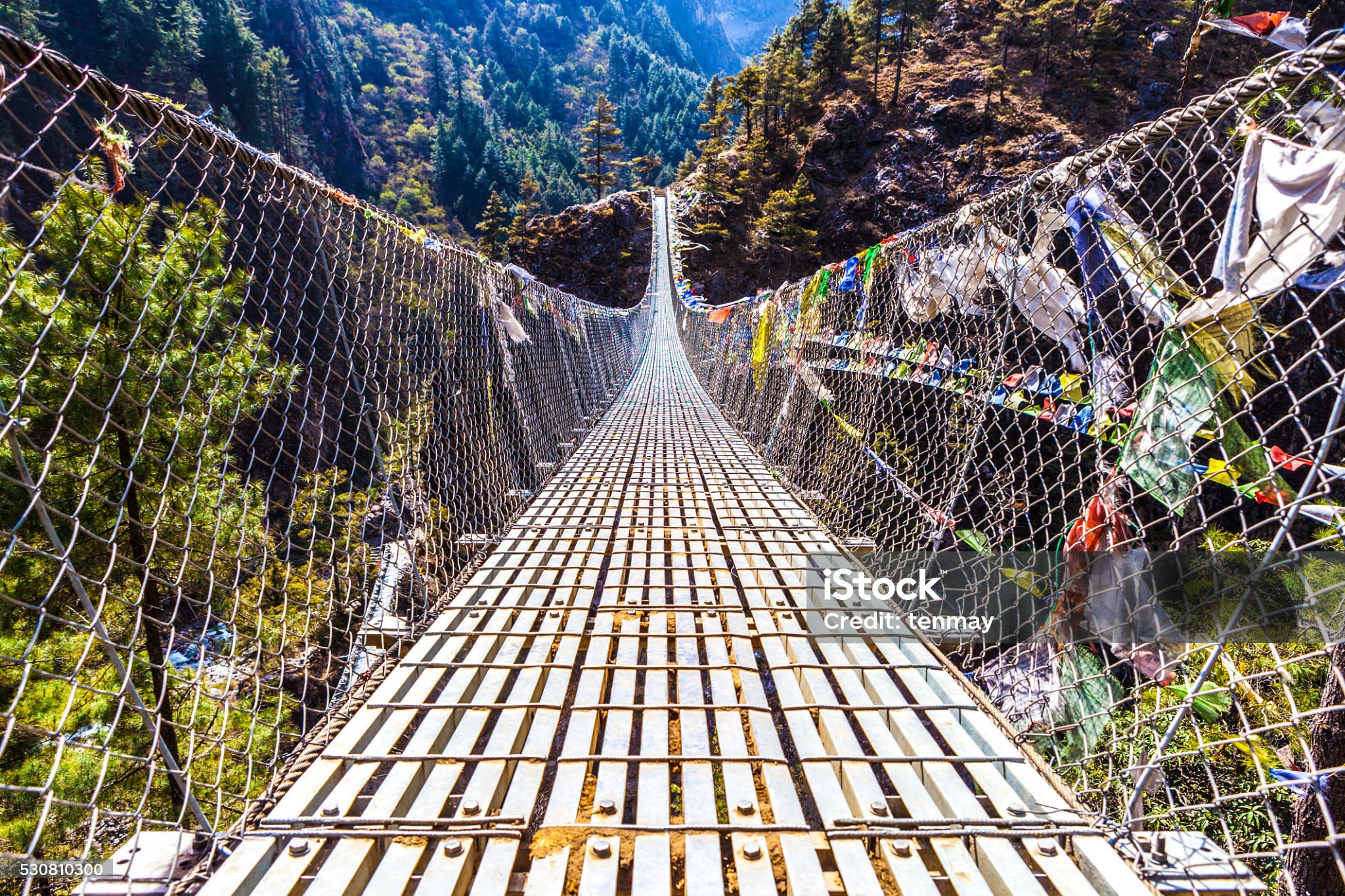 Low angle view of the Dughla Waterfall suspension footbridge with prayer flags located in the Lobuche Valley, Nepal.
