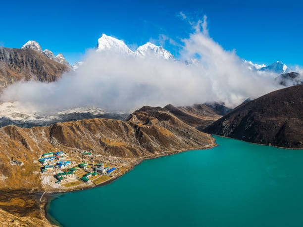 Deep blue high altitude skies above the snowy summits of Cholatse (6440m) and Taboche (6542m), rising through the clouds covering the Ngozumpa glacier and Gokyo deep in the remote Himalayan mountain wilderness of the Everest National Park on the Nepal Tibet border, a UNESCO World Heritage Site.
